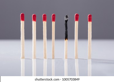 Burnt Matchstick Separated By Red Matchsticks Against Grey Background