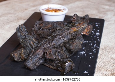 Burnt Meat Dish With Potatoes And Sauce On Black Stone Plate