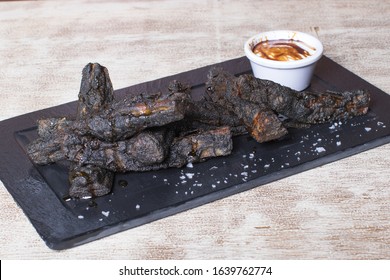 Burnt Meat Dish With Potatoes And Sauce On Black Stone Plate