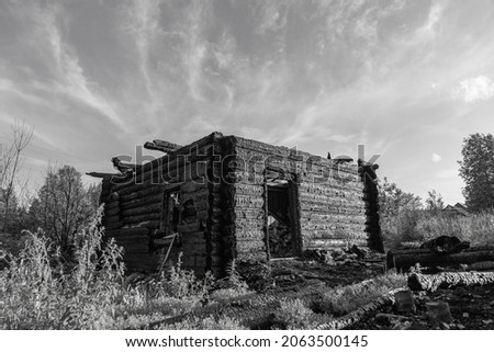 Burnt old log house in a village on a summer day against a gray sky. Black and white image. Close-up