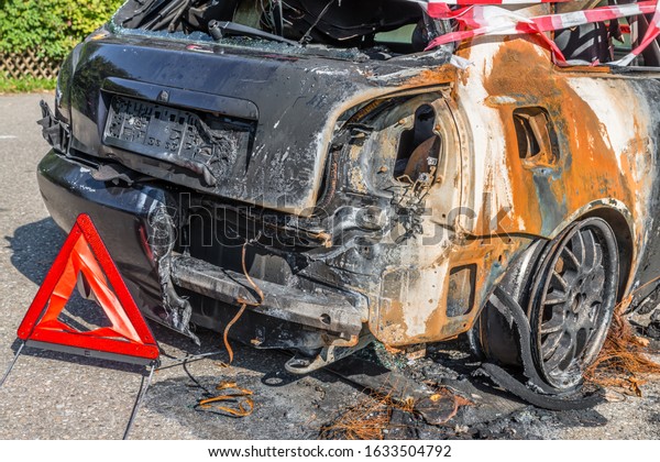 Burnt out car after a violent accident with\
police barrier tape in red and white with the German word for\
police barricade, Germany
