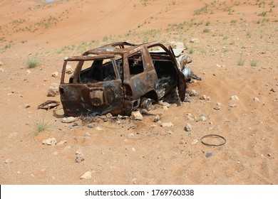 Burnt out and rusting wreckage of a 4WD (four wheel drive) vehicle partially buried in remote arid desert sand dunes in Sharjah, United Arab Emirates. The desert sand is slowly covering the wreckage.