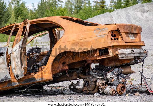 Burnt\
out scrapped car left in a gravel pit near\
nature.