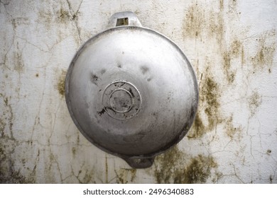 A burnt pan made of aluminum hung against a dirty wall - Powered by Shutterstock