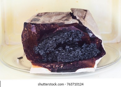 Burnt Paper Bag With Melted And Burnt Popcorn In The Greased And Dirty Microwave Oven, After The Explosion And Fire 