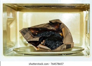 Burnt Paper Bag With Melted And Burnt Popcorn In The Greased And Dirty Microwave Oven, After The Explosion And Fire