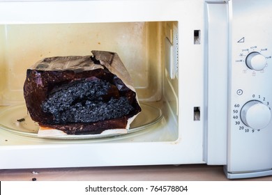 Burnt Paper Bag With Melted And Burnt Popcorn In The Greased And Dirty Microwave Oven, After The Explosion And Fire 