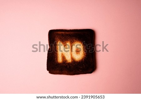 burnt slice of white bread toast with the word No on it on pink  background passionate ardent disagreement. poster creative rejection concept composition 