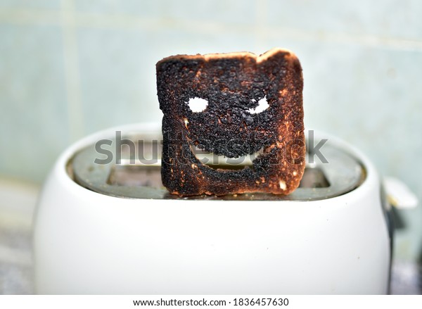 Burnt toast with an angry face expressing the\
emotion of sadness or sarcasm. Burnt toast bread slices out of a\
toaster. Сoncept of unsuccessful breakfast preparation before a\
work day or weekend