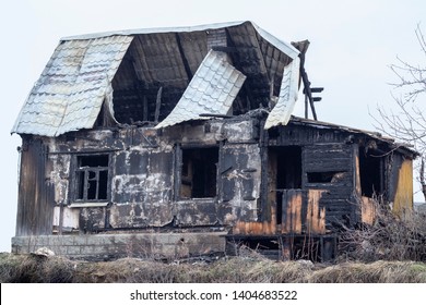 Burnt wooden house, black charred skeleton of a country house. Charred logs remained from the village house. Charred walls, empty windows and hollow roof after a fire - Powered by Shutterstock