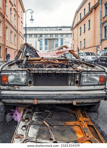 A burnt-out, rusted-out car on the street\
of a European city, vertical\
photo