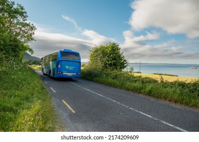 Burren, Ireland - 06.22.2022: Blue Passenger Bus With TFI Transport For Ireland Logo On A Side And Bus Eireann Sign On A Small Narrow Country Road. Transportation Industry. Commute To Rural Area