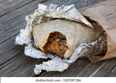Burrito With A Bite Out Of It In Foil And Paper Sack