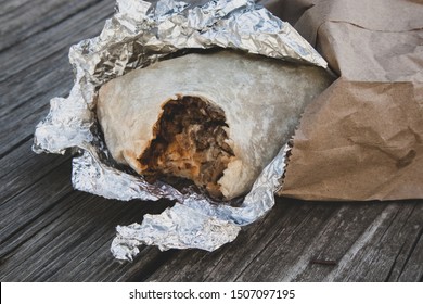 Burrito With A Bite Out Of It In Foil And Paper Sack