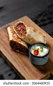 burrito mexican food with meat in pita bread on a piece of wood with sour cream sauce