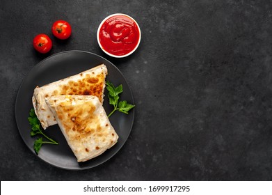 Burrito wraps with chicken and vegetables 
in a black plate , against a background of concrete 
with copy space for your text, 
Mexican 