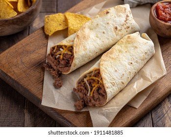 Burritos with ground beef, refried beans and cheese on a wooden cutting board