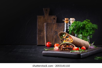 Burritos wraps with beef and vegetables on  dark wooden background. Beef burrito, mexican food.