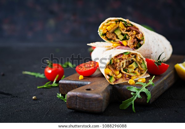 Burritos wraps with beef and vegetables on \
black background. Beef burrito, mexican\
food.