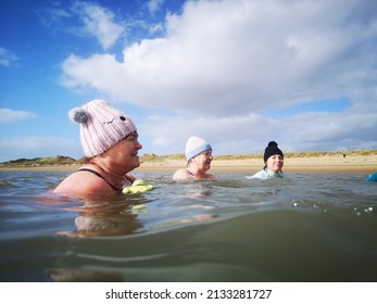 Burry Port, Wales, UK: February 25, 2022: A Small Group Of Ladies Swim In Open Sea Water During The Winter Months For Physical And Mental Health Benefits. They Are Wearing Wetsuits And Bobble Hats To 