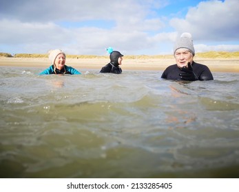 Burry Port, Wales, UK: February 25, 2022: A Small Group Of Ladies Swim In Open Sea Water During The Winter Months For Physical And Mental Health Benefits. They Are Wearing Wetsuits And Bobble Hats To 