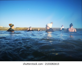 Burry Port, Wales, UK: January 13, 2022: A Small Group Of Ladies Swim In Open Sea Water During The Winter Months For Physical And Mental Health Benefits. They Are Wearing Wetsuits And Bobble Hats To 