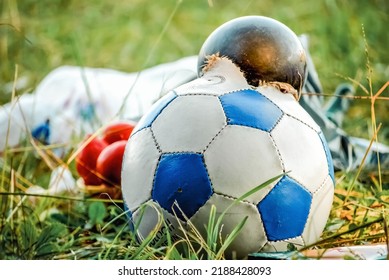 Burst soccer ball lies in pile of garbage on green grass in city. Torn ball thrown as rubbish after playing football game close view - Powered by Shutterstock