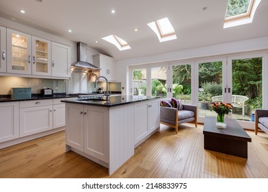 Burwell, Cambridgeshire, England - October 13 2016: Modern Furnished Kitchen With Island, Seating And Bifold Doors Leading To Patio Garden