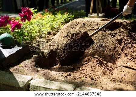 Burying grave. Funeral details. Mourning ceremony. Gravedigger with shovel. Burial of body.