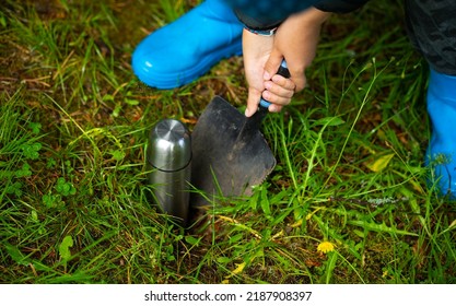 Burying the treasure in the garden. A child buries a metal bottle with coins in the ground. Hide the treasure. A time capsule in the ground. A message to the future. - Shutterstock ID 2187908397