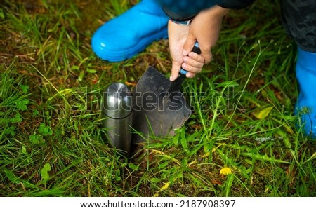 Burying the treasure in the garden. A child buries a metal bottle with coins in the ground. Hide the treasure. A time capsule in the ground. A message to the future.