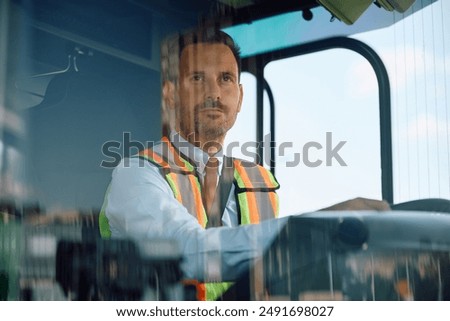 Bus driver driving in reverse while looking in rear view mirror. The view is through the windshield. 