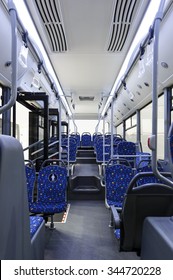 Bus Inside, City Transportation White Interior With Blue Seats In Row, Retirement Places, Open Doors, Handles For Standing Passengers, Bright Lights And Air Conditioner 