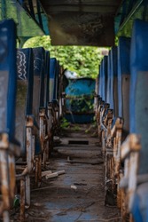 A Bus With Old, Rusted Seats And A Dirty Floor. The Seats Are Empty, And The Bus Appears To Be Abandoned. Scene Is One Of Decay And Neglect
