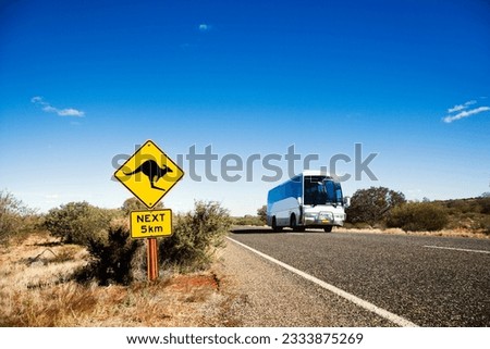 Bus on two lane asphalt road in rural Australia with kangaroo crossing sign.