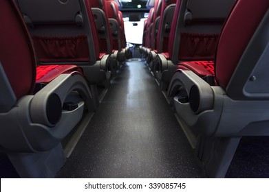 Bus seats in row with red leather and textile coating, wooden armrests and mounts for safety belts, rear view, modern comfortable tourist transport interior, selective focus 