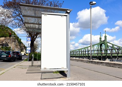 Bus Shelter And Bus Stop On Urban Street In Europe. Empty Blank White Ad Space. Old City Street Backgroind With Steel Suspension Bridge. Poster Ad Display. Banner And Copy Space. Base Photo For Mockup