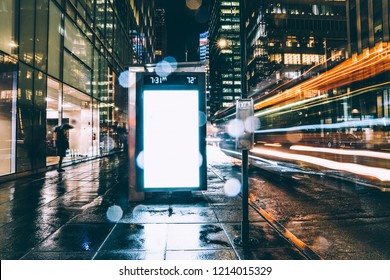 Bus Station Billboard In Rainy Night With Blank Copy Space Screen For Advertising Or Promotional Content, Empty Mock Up Lightbox For Information, Clear Display In Urban City Street With Long Exposure