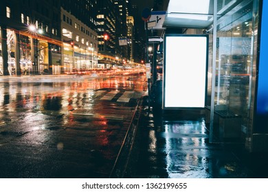 Bus Station Billboard In Rainy Night With Blank Copy Space Screen For Advertising Or Promotional Content, Empty Mock Up Lightbox For Information, Blank Display In Urban City Street With Long Exposure