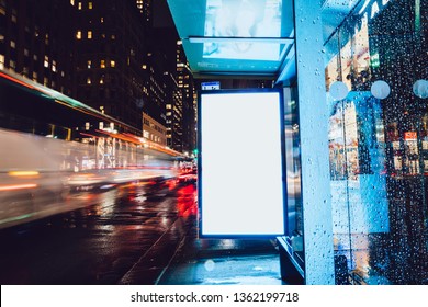 Bus Station Billboard In Rainy Night With Blank Copy Space Screen For Advertising Or Promotional Content, Empty Mock Up Lightbox For Information, Blank Display In Urban City Street With Long Exposure