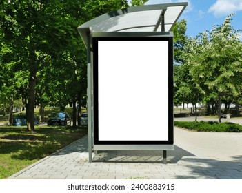 bus stop with blank white poster ad lightbox. bus shelter advertising concept. glass and aluminum. commercial poster space and display panel. green urban street. lush foliage. soft background