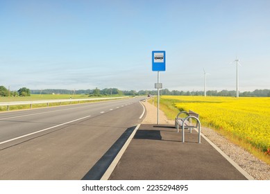 Bus stop and country highway (new asphalt road) through the green forest meadow and blooming yellow rapeseed field at sunrise. Fog, soft sunlight. Transportation, remote places, vacations concepts - Shutterstock ID 2235294895