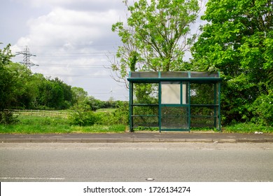 Bus Stop On The Side Of A Lane/road, In The Countryside, Or Rural Area. Bus Stop Is Empty. It's A Sunny Summer Day, With A Blue Sky In The Background. There's Green Grass And Trees.