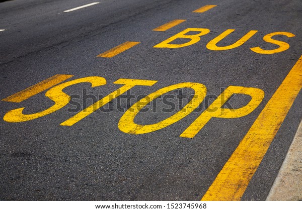 Bus stop sign with yellow paint on\
the asphalt. A symbol of expectation, rethinking the meaning of\
life, the final path, the road to the\
future.