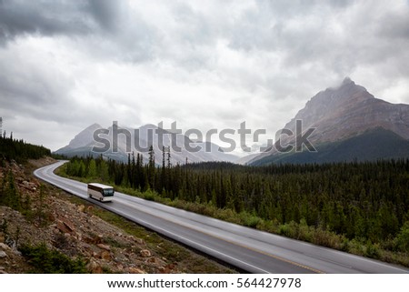 Bus traveling on a scenic highway in Banff National Park with mountains in the background. Picture taken during a cloudy summer morning in Alberta, Canada.