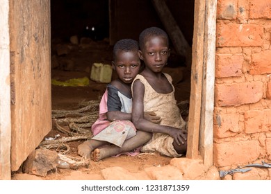 Busagazi, Uganda. May 03 2017. Two Ugandan children in ragged clothes sitting in an embrace on a dirt floor at the doorstep of a house. Busagazi village is on the shore of Lake Victoria.