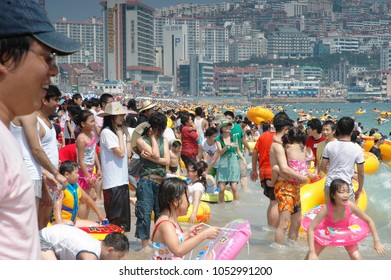 Busan, South Korea, Summer: A Very Large Big Crowd Of People On The Beach During The Summer By The Ocean. Skyscrapers In The Background.