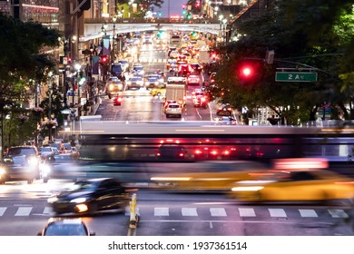 Buses and taxis driving through a busy intersection 42nd Street through Midtown Manhattan in New York City at night 