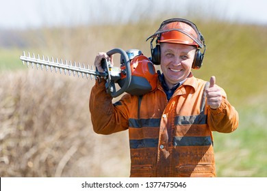 Bush trimming work. Shrubs pruning. Happy Landscaper Man Worker in uniform with Hedge Trimmer Tool gersturing Ok sign