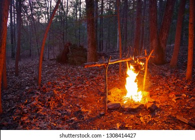 Bushcraft Campfire For Cooking. Debris Hut Primitive Survival Shelter In The Background